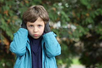 Autism concept. Lonely little boy covering his ears outdoors, space for text