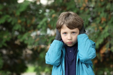 Photo of Autism concept. Lonely little boy covering his ears outdoors, space for text