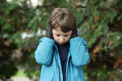 Autism concept. Lonely little boy covering his ears outdoors