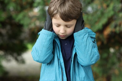 Autism concept. Lonely little boy covering his ears outdoors