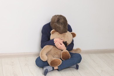 Autism concept. Lonely little boy with teddy bear on floor at home