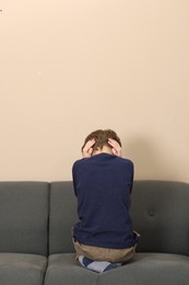 Autism concept. Lonely little boy covering his ears on sofa at home, back view