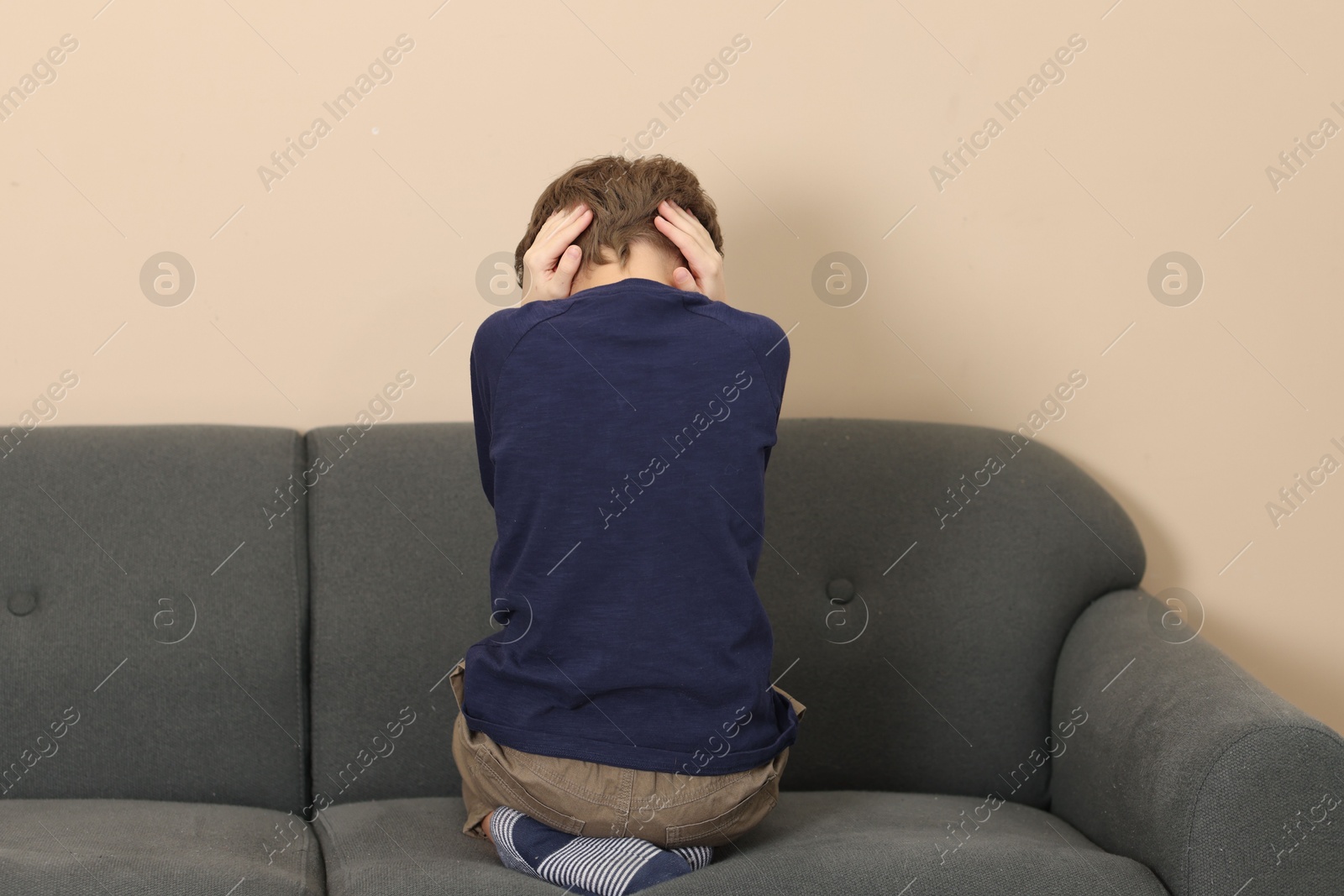 Photo of Autism concept. Lonely little boy covering his ears on sofa at home, back view