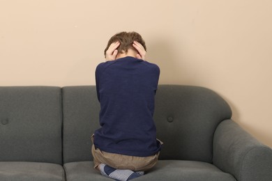 Autism concept. Lonely little boy covering his ears on sofa at home, back view