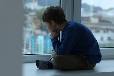 Autism concept. Lonely little boy near window at home