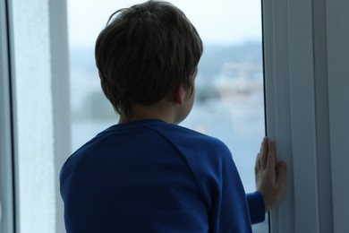 Autism concept. Lonely little boy near window at home, back view