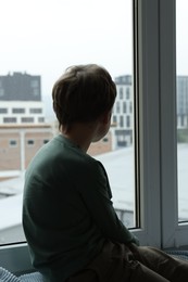 Photo of Autism concept. Lonely little boy near window at home