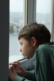 Autism concept. Lonely little boy near window at home