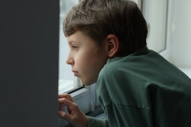 Autism concept. Lonely little boy near window at home