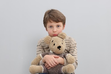 Autism concept. Lonely little boy with teddy bear on grey background