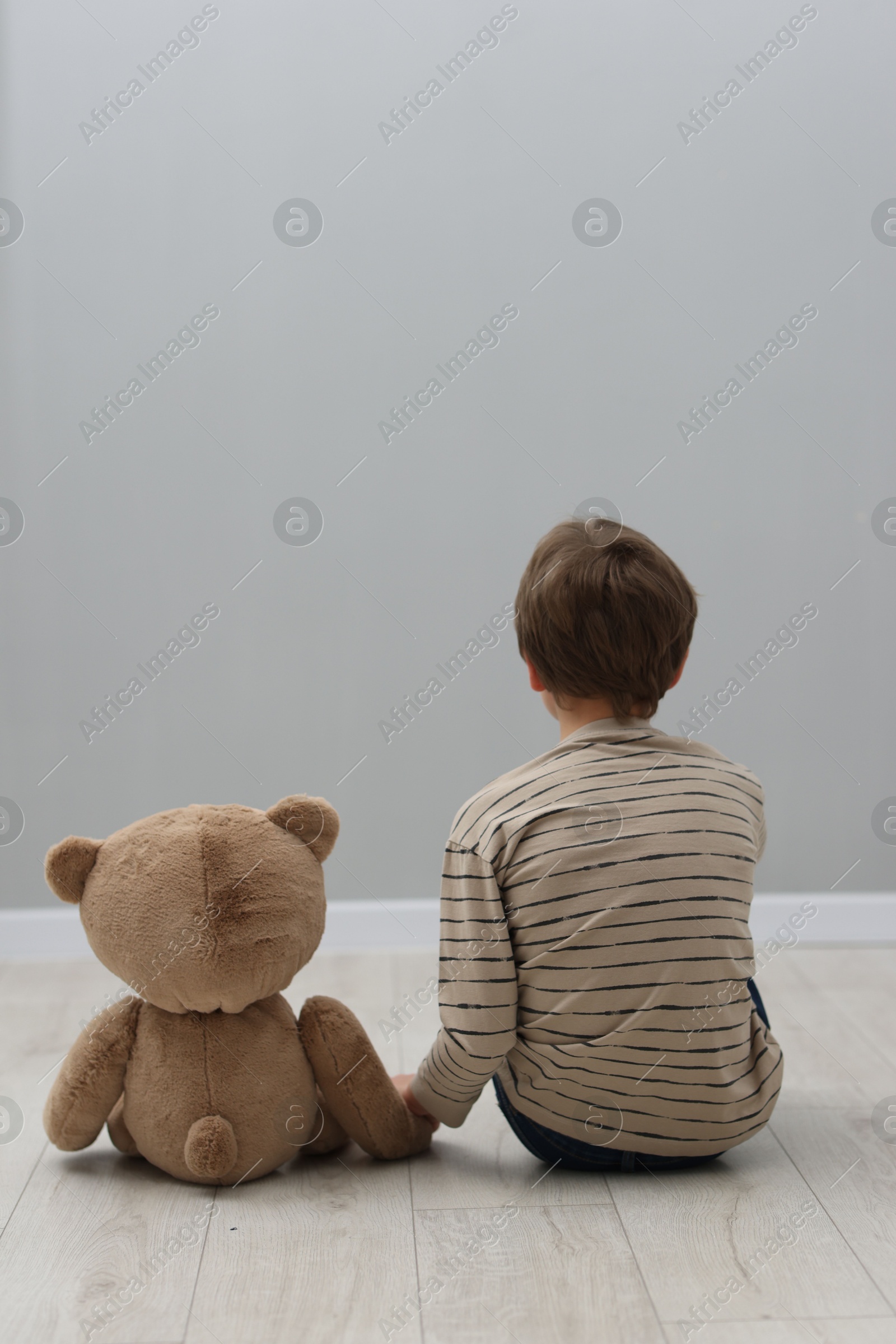 Photo of Autism concept. Lonely little boy with teddy bear on floor at home, back view