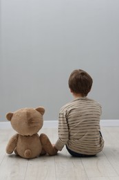 Autism concept. Lonely little boy with teddy bear on floor at home, back view