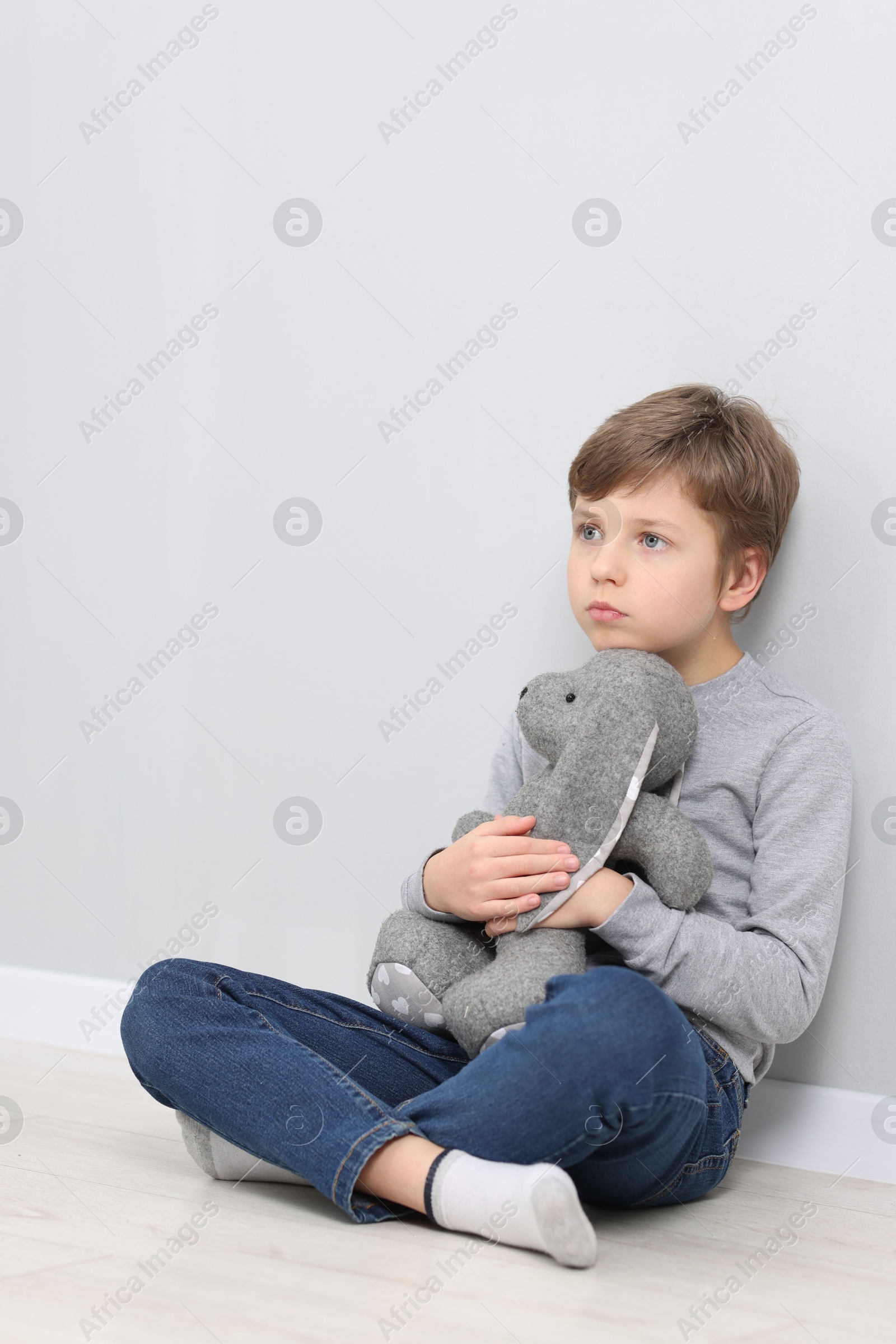 Photo of Autism concept. Lonely little boy with toy bunny on floor near grey wall at home