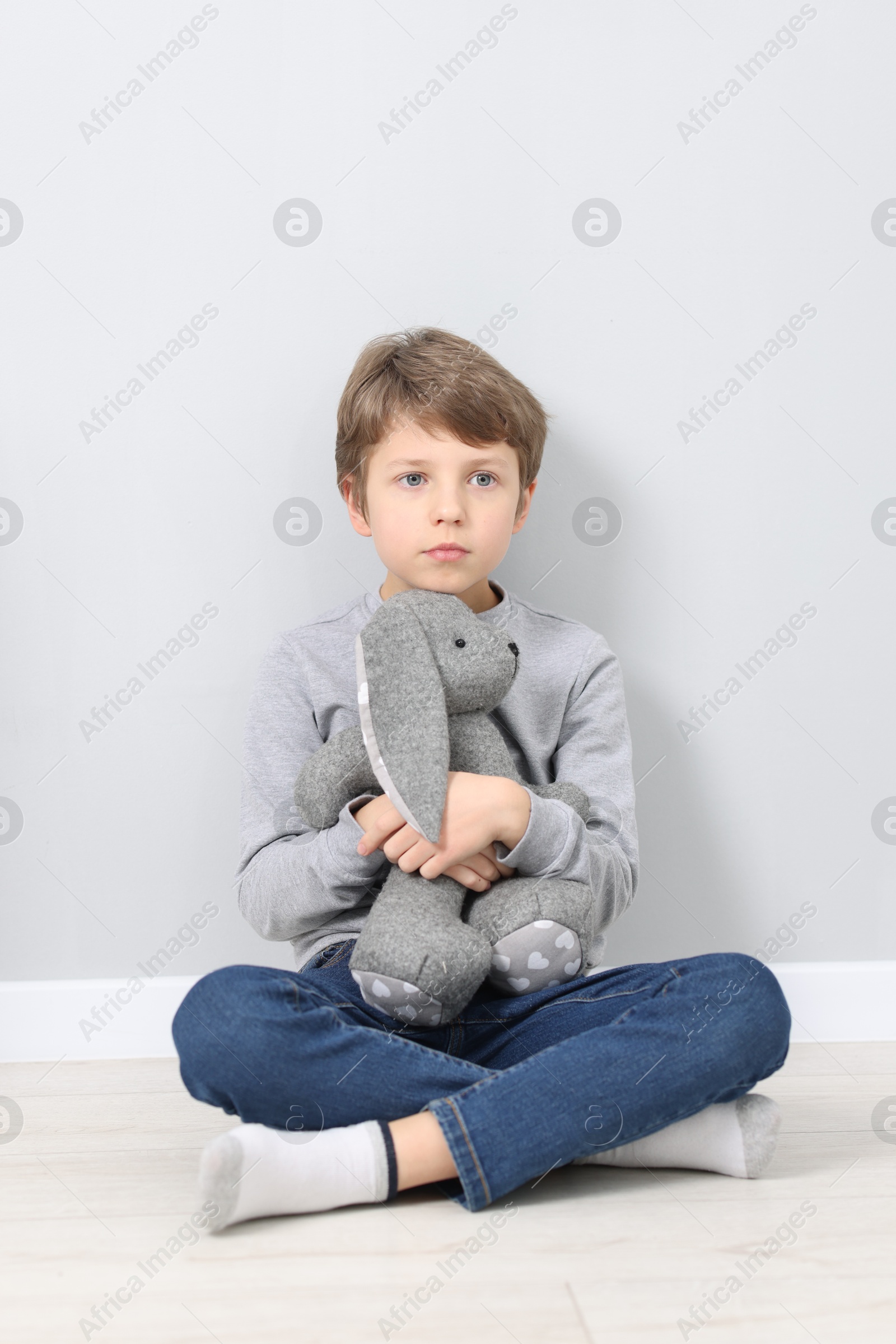 Photo of Autism concept. Lonely little boy with toy bunny on floor near grey wall at home