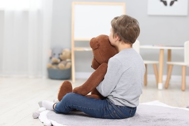 Autism concept. Lonely little boy with teddy bear on floor at home