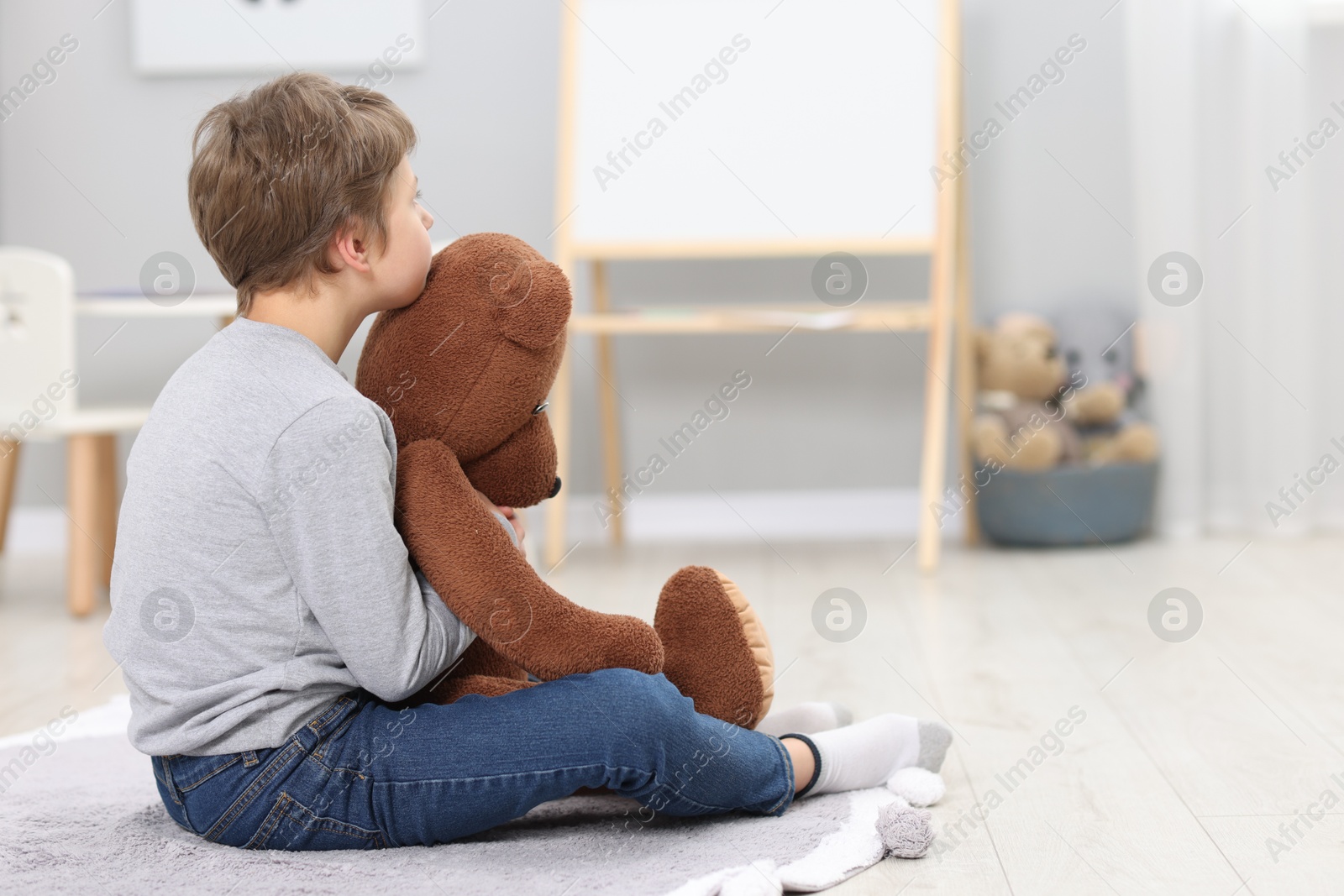 Photo of Autism concept. Lonely little boy with teddy bear on floor at home, space for text