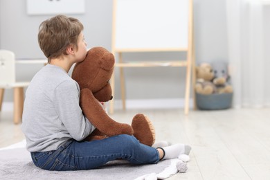 Photo of Autism concept. Lonely little boy with teddy bear on floor at home, space for text