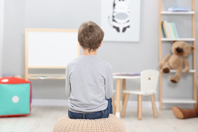 Photo of Autism concept. Lonely little boy on pouffe at home, back view