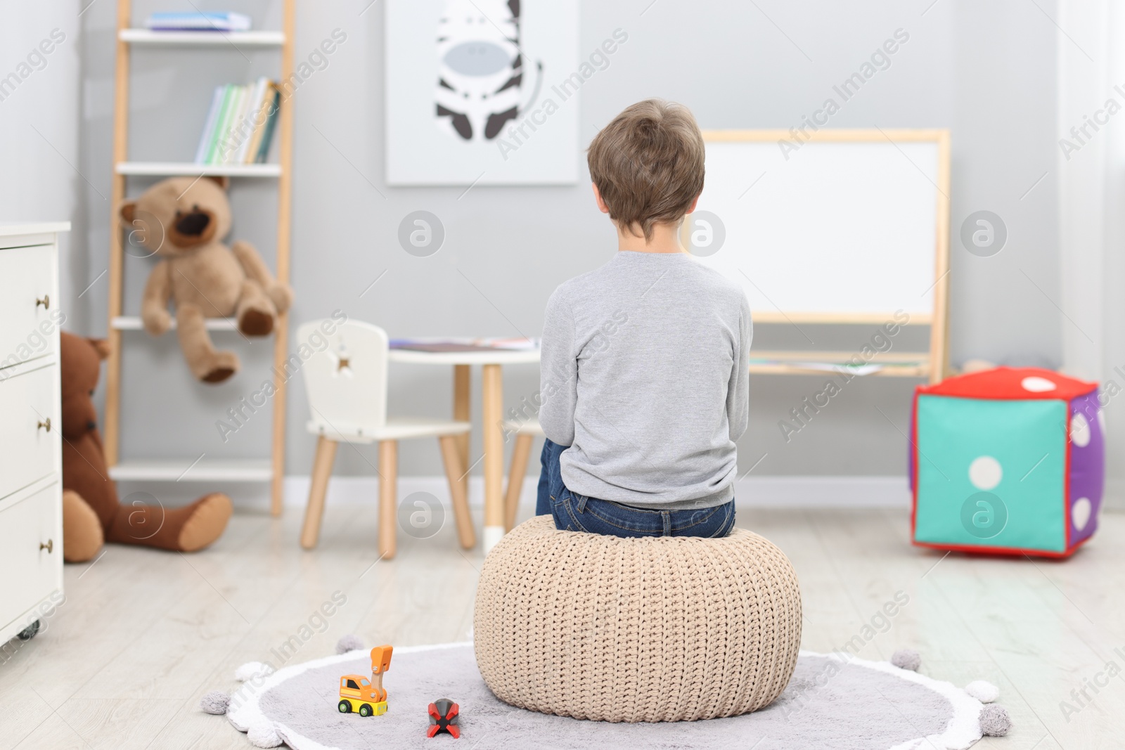 Photo of Autism concept. Lonely little boy on pouffe at home, back view