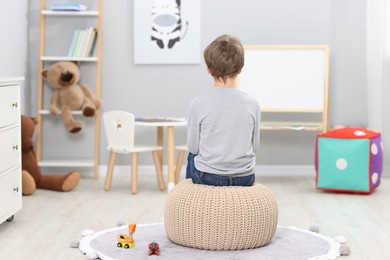 Autism concept. Lonely little boy on pouffe at home, back view