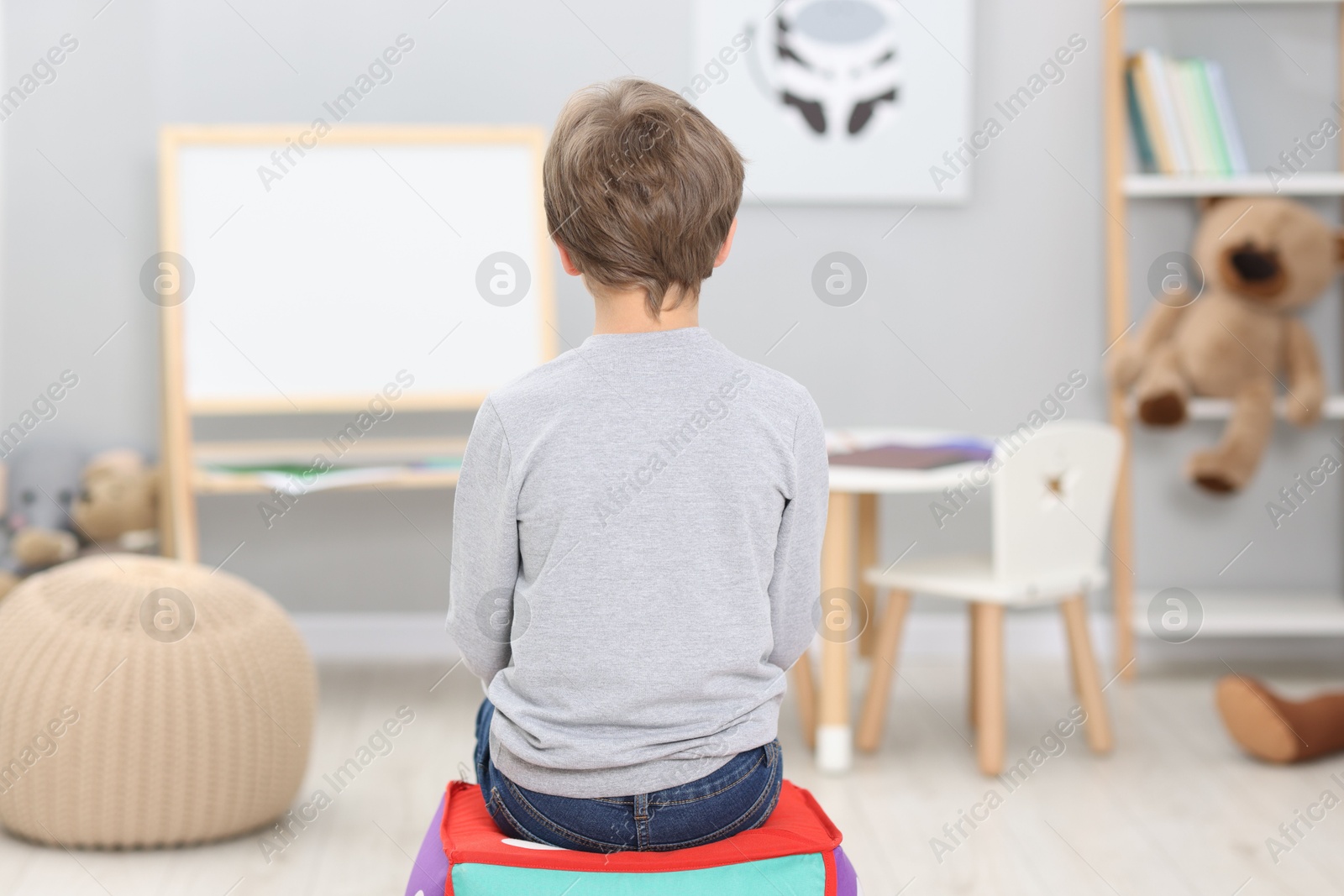 Photo of Autism concept. Lonely little boy on pouffe at home, back view