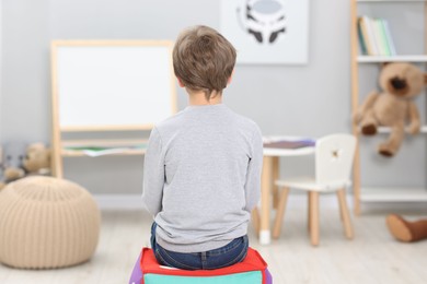 Autism concept. Lonely little boy on pouffe at home, back view