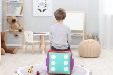 Autism concept. Lonely little boy on pouffe at home, back view