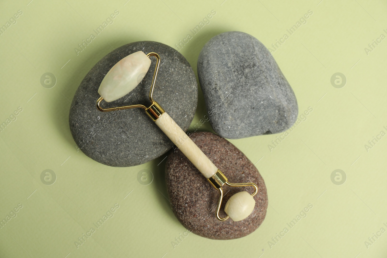 Photo of Face roller and stones on light green background, top view