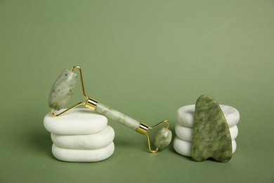 Photo of Face roller, gua sha tool and massage stones on green background