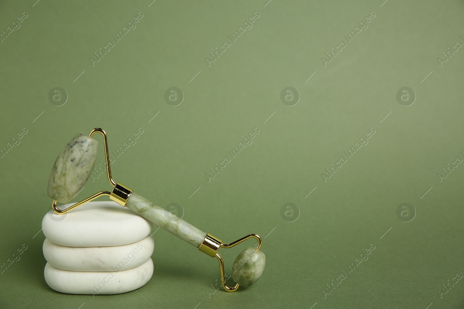 Photo of Face roller and massage stones on green background. Space for text