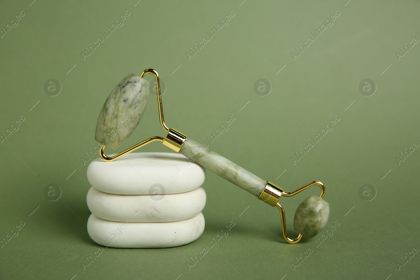 Photo of Face roller and massage stones on green background