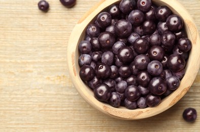 Photo of Ripe acai berries in bowl on wooden table, top view. Space for text