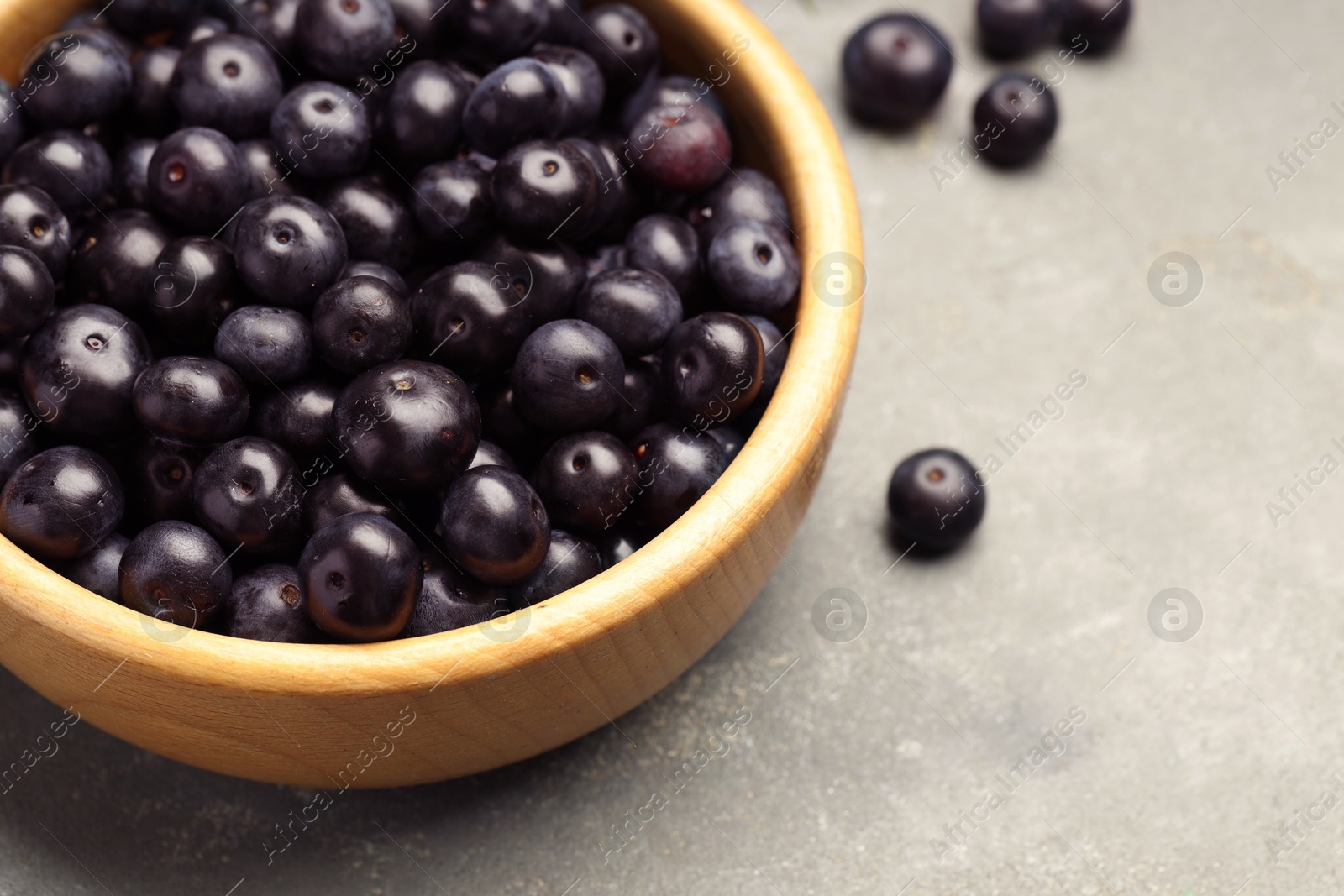 Photo of Ripe acai berries in bowl on grey textured table, closeup. Space for text