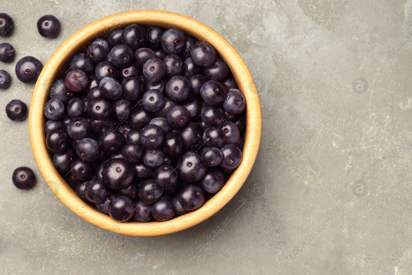 Photo of Ripe acai berries in bowl on grey textured table, top view. Space for text