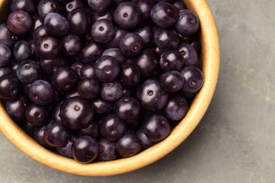 Photo of Ripe acai berries in bowl on grey textured table, top view. Space for text