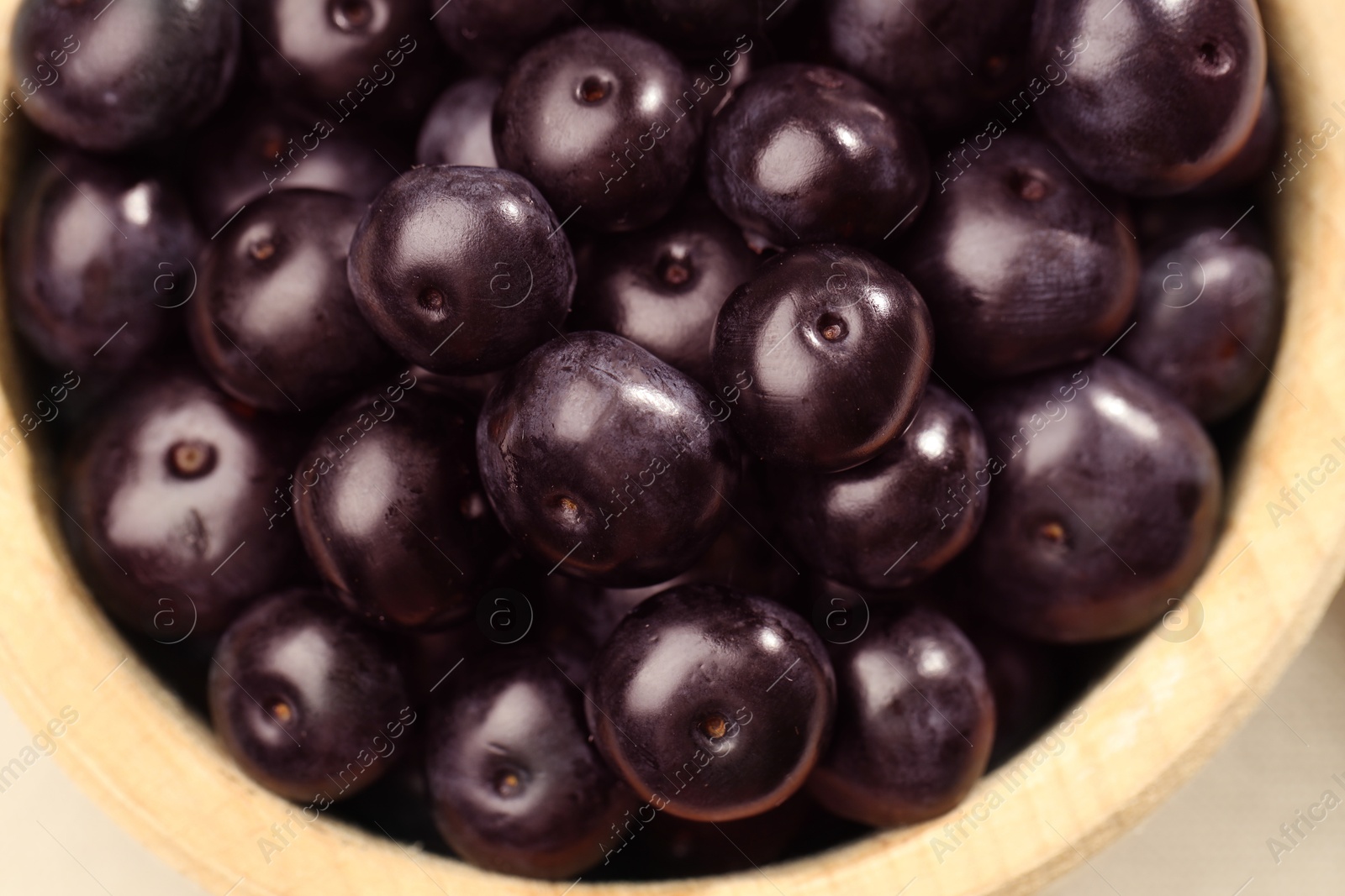 Photo of Ripe acai berries in wooden bowl, top view