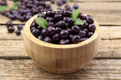 Photo of Ripe acai berries and leaves in bowl on wooden table, closeup