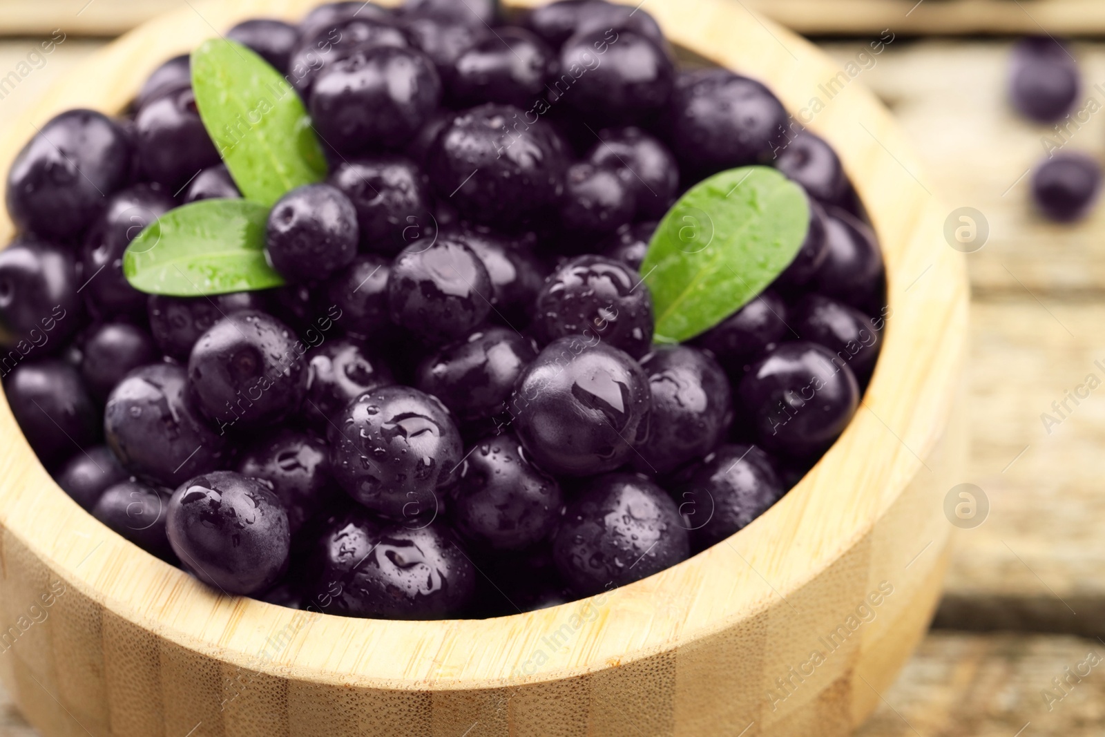 Photo of Ripe acai berries and leaves in bowl on table, closeup