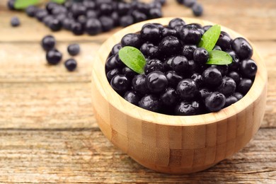 Photo of Ripe acai berries and leaves in bowl on wooden table, closeup. Space for text