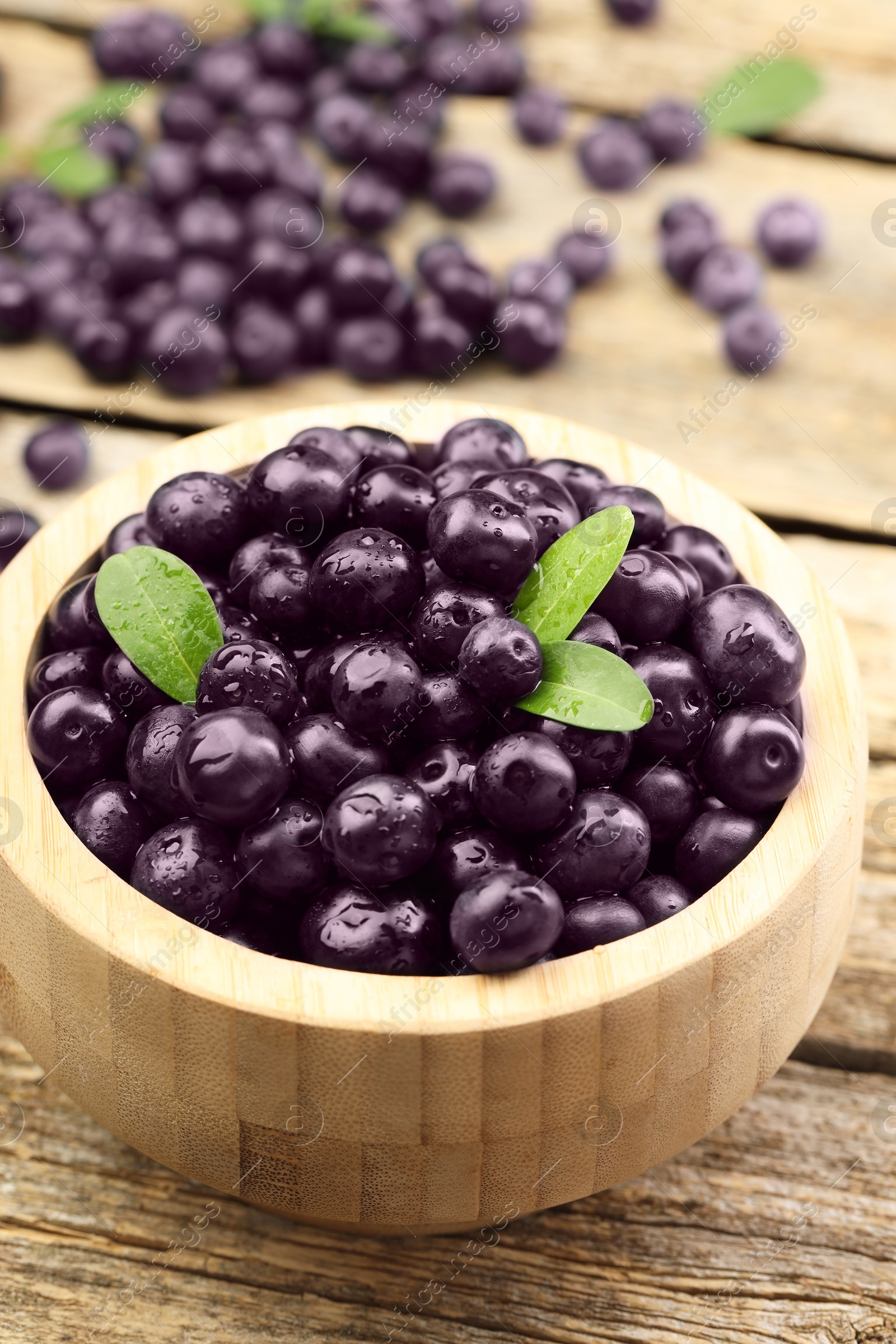 Photo of Ripe acai berries and leaves in bowl on wooden table