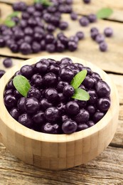 Photo of Ripe acai berries and leaves in bowl on wooden table