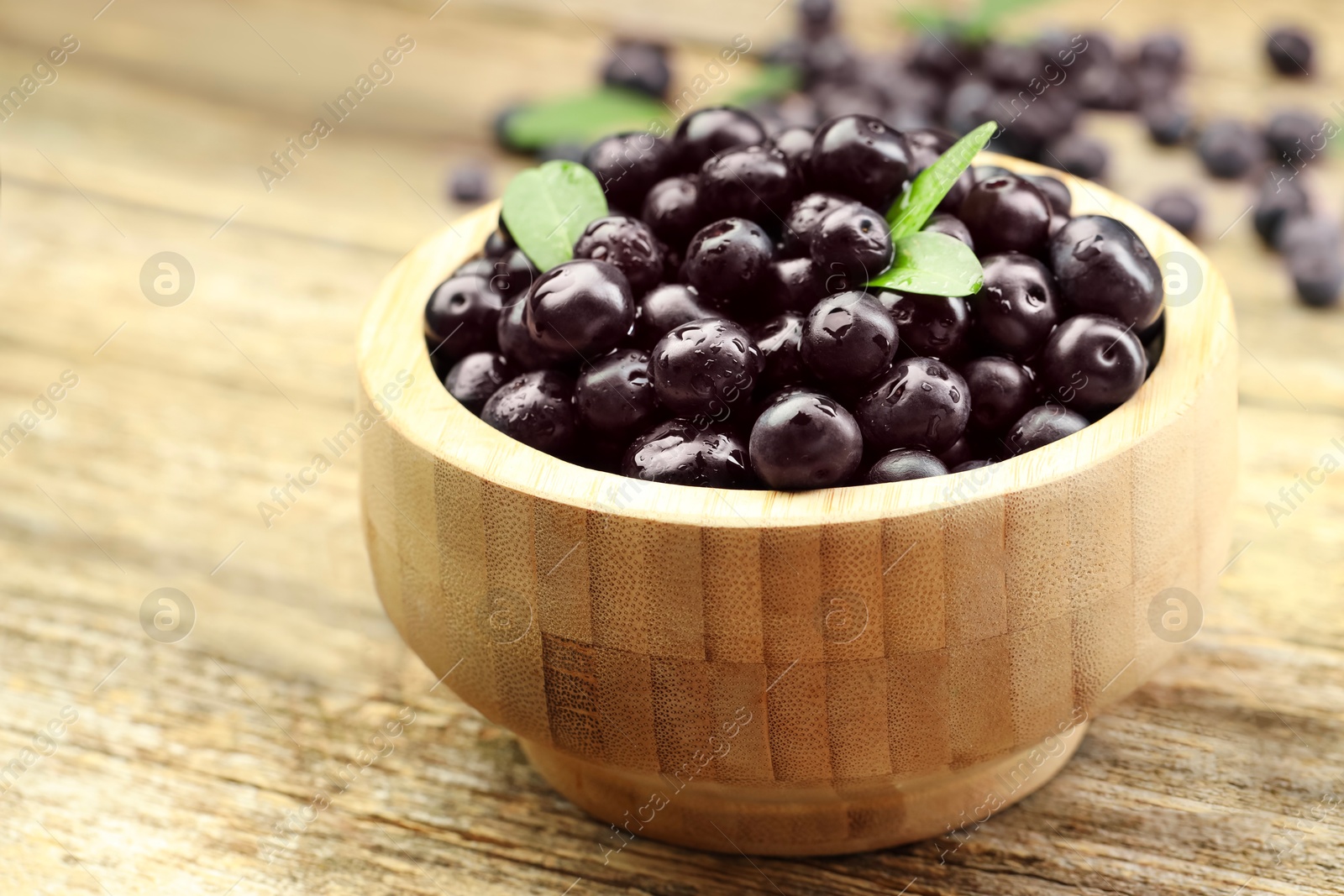 Photo of Ripe acai berries and leaves in bowl on table, closeup