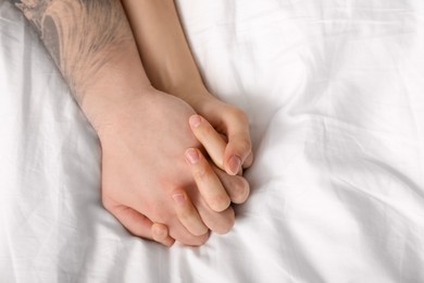 Photo of Lovely couple holding hands in bed, top view. Space for text