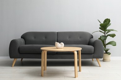 Photo of Comfortable sofa, houseplant and table near grey wall in room