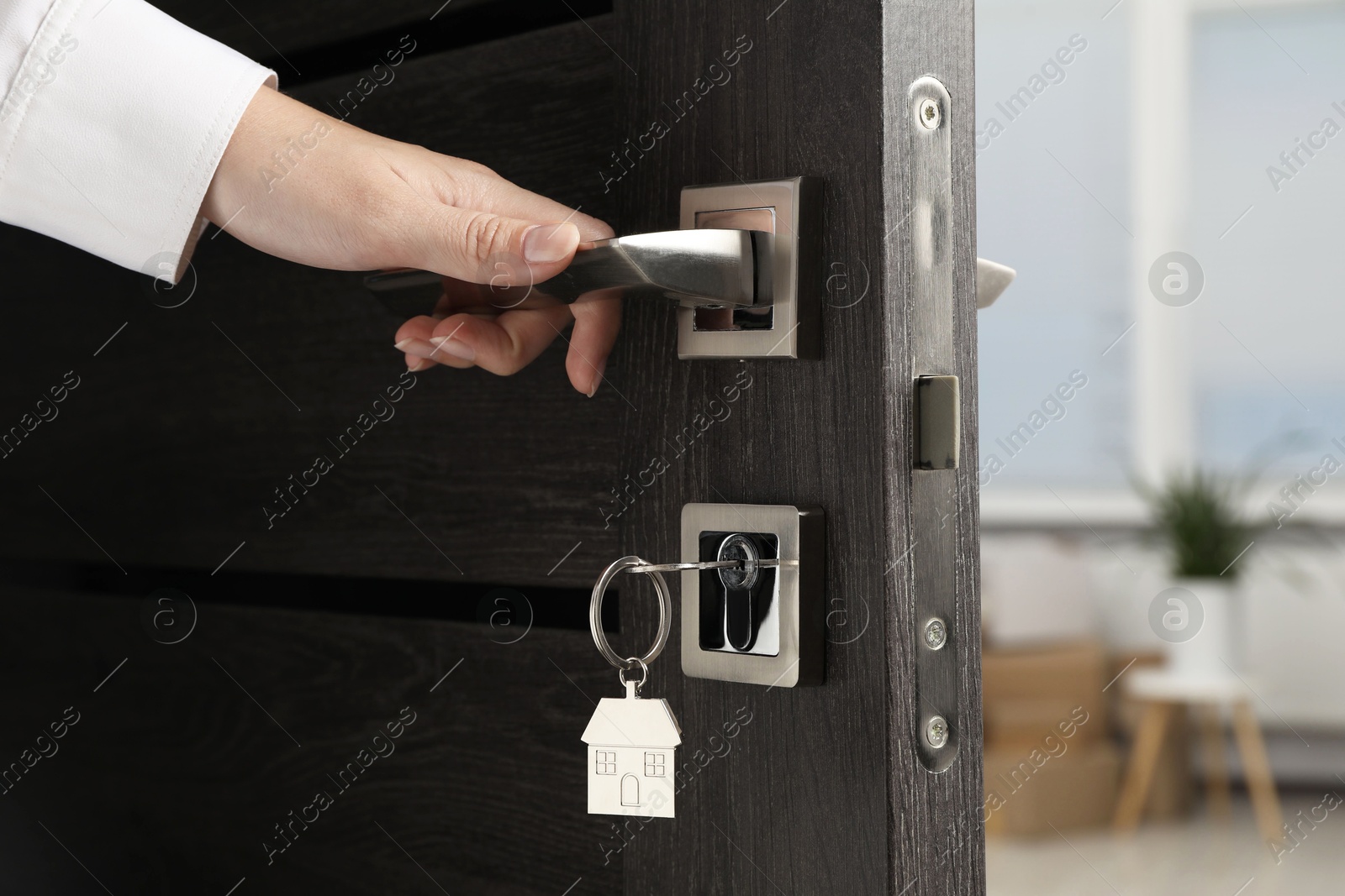 Photo of Woman opening door with key and house shaped keychain, closeup