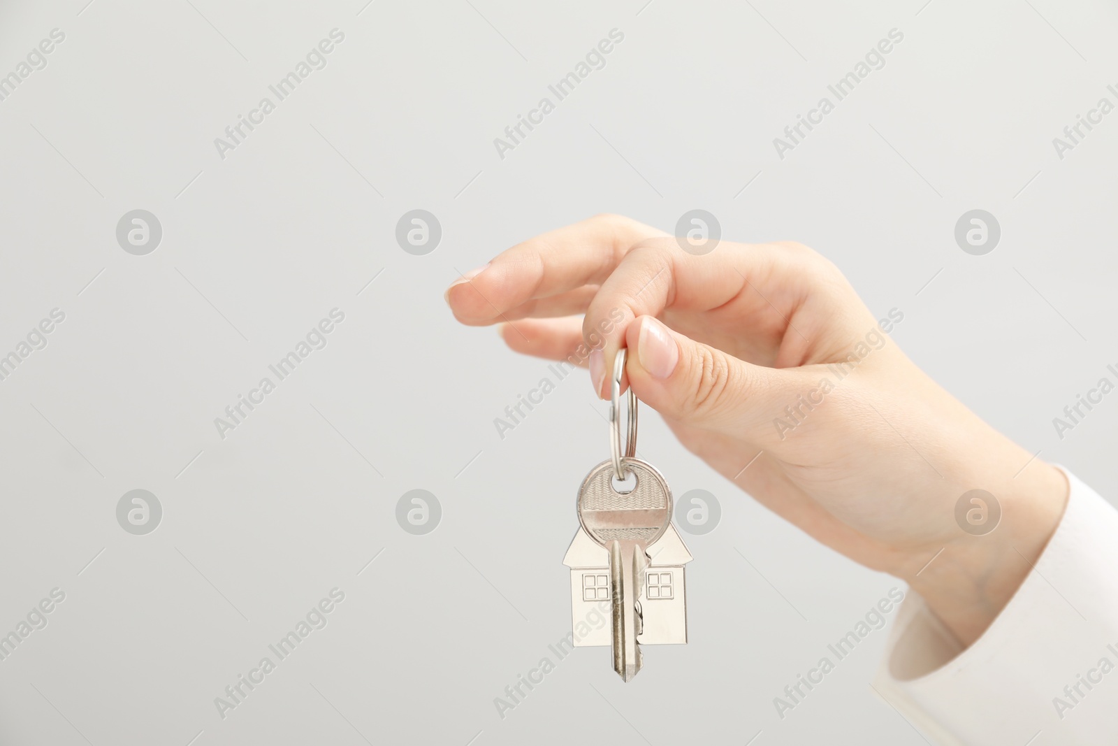 Photo of Woman holding key with keychain on light grey background, closeup. Space for text