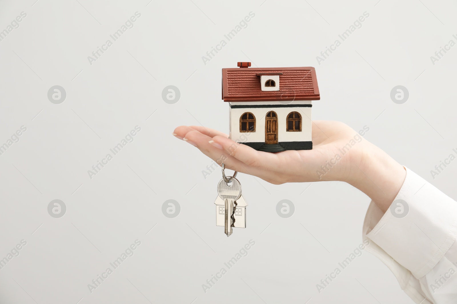 Photo of Woman holding key with keychain and house model on light grey background, closeup