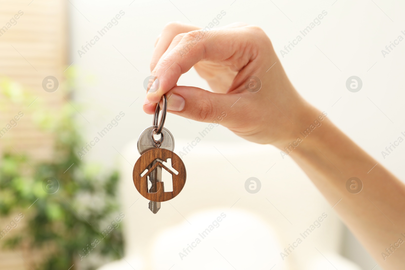 Photo of Woman holding key with house shaped keychain indoors, closeup