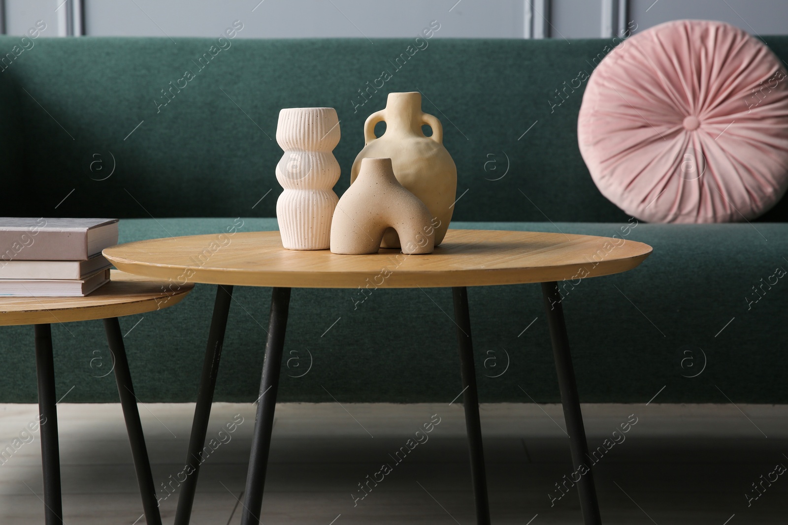 Photo of Stylish sofa with cushion, books and decor elements on nesting tables in room