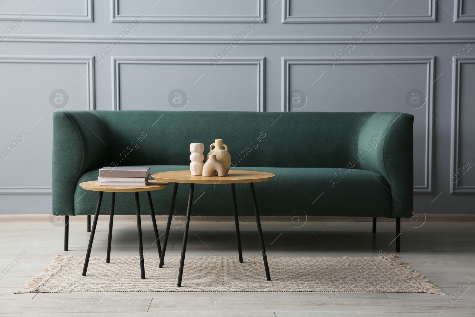 Photo of Stylish sofa, books and decor elements on nesting tables in room